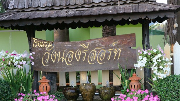 A wooden structure with a signboard, surrounded by potted plants and flowers. - Wangnong Resort (Ubon Ratchathani)