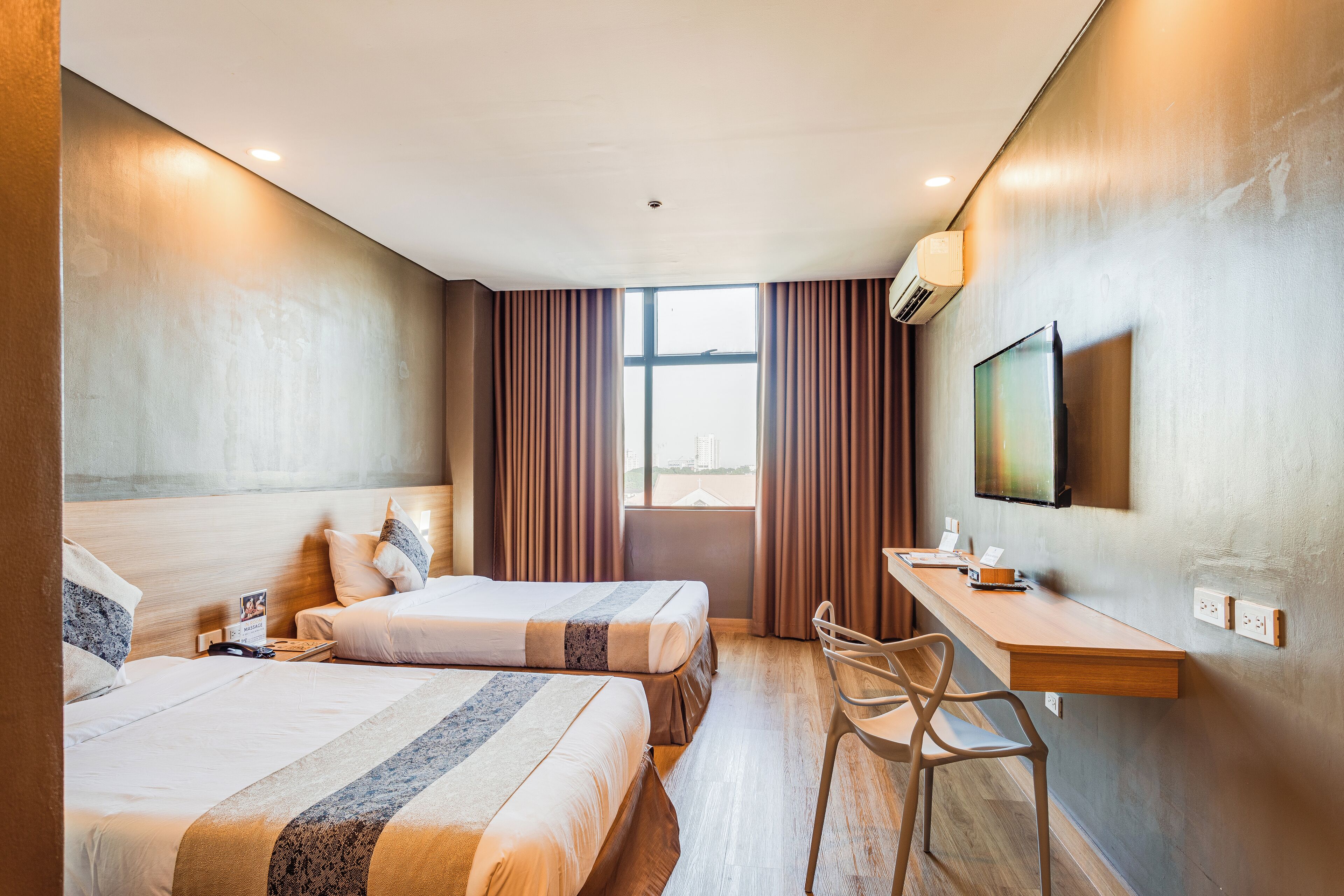 Une chambre d’hôtel avec deux lits, un bureau, une chaise, une télévision et une fenêtre avec des rideaux.