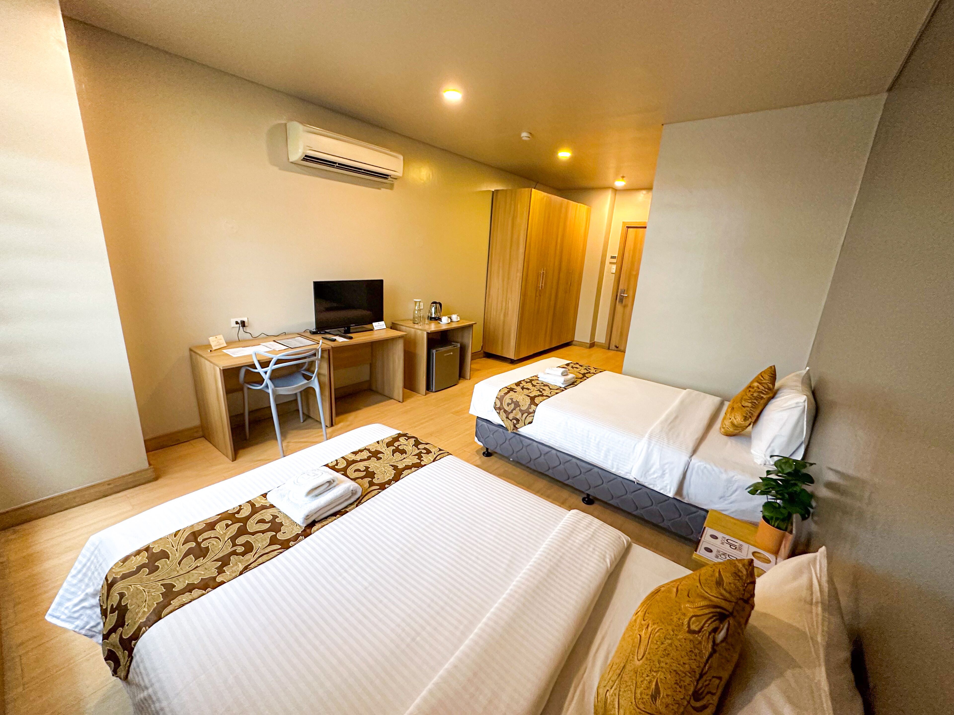 A hotel room with two beds, a desk with a computer, a television, and an air conditioning unit.