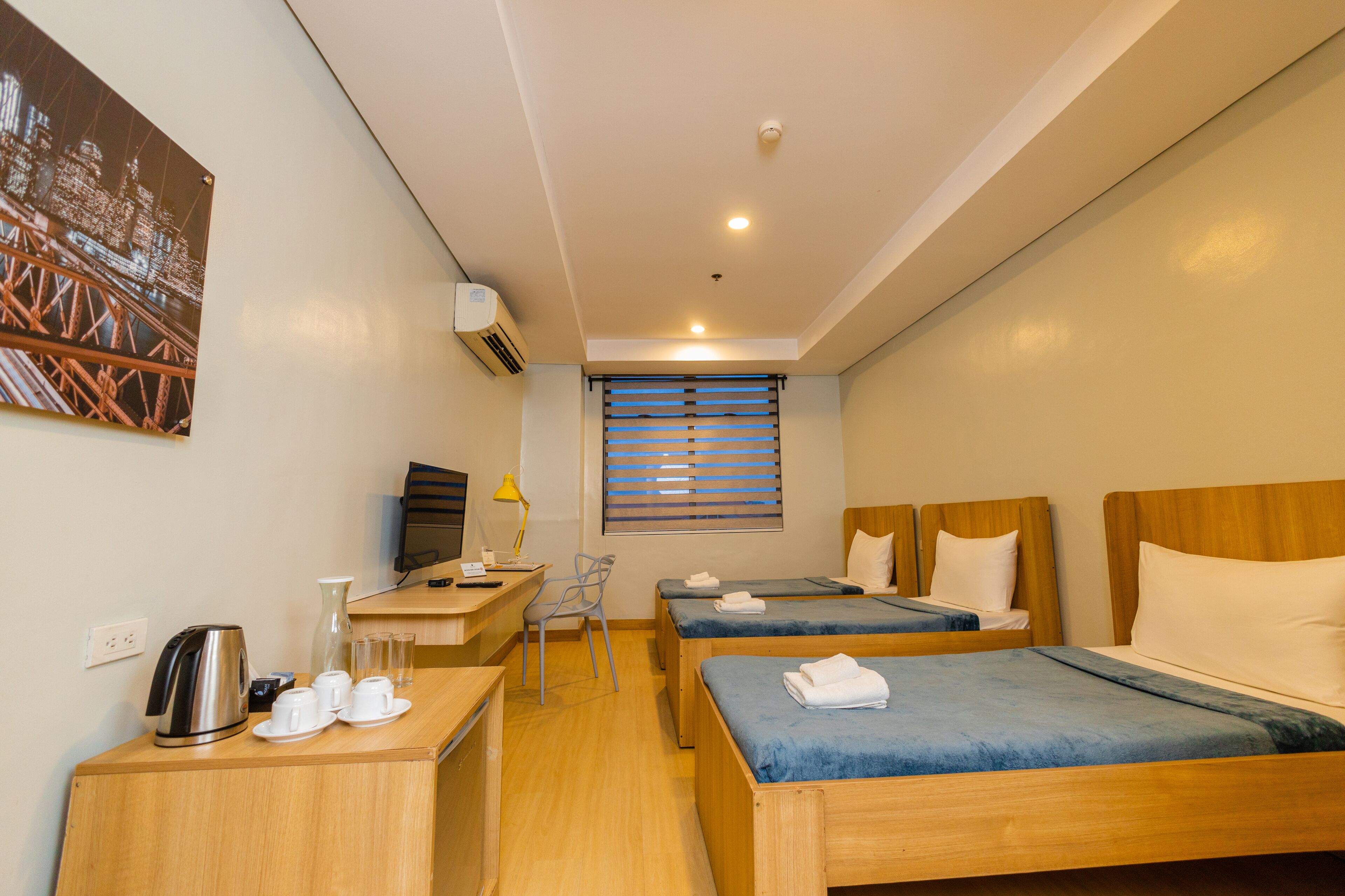 A hotel room with two beds, a desk, a chair, a TV, and a window with blinds.