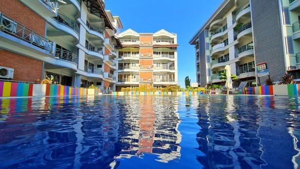 A swimming pool with multi-story buildings on either side, featuring balconies and a clear blue sky. - Perdana Serviced Apartment & Resorts (Langkawi)