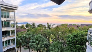A multi-story building with balconies overlooking a landscaped area with palm trees and a view of the sea. - Perdana Serviced Apartment & Resorts (Langkawi)