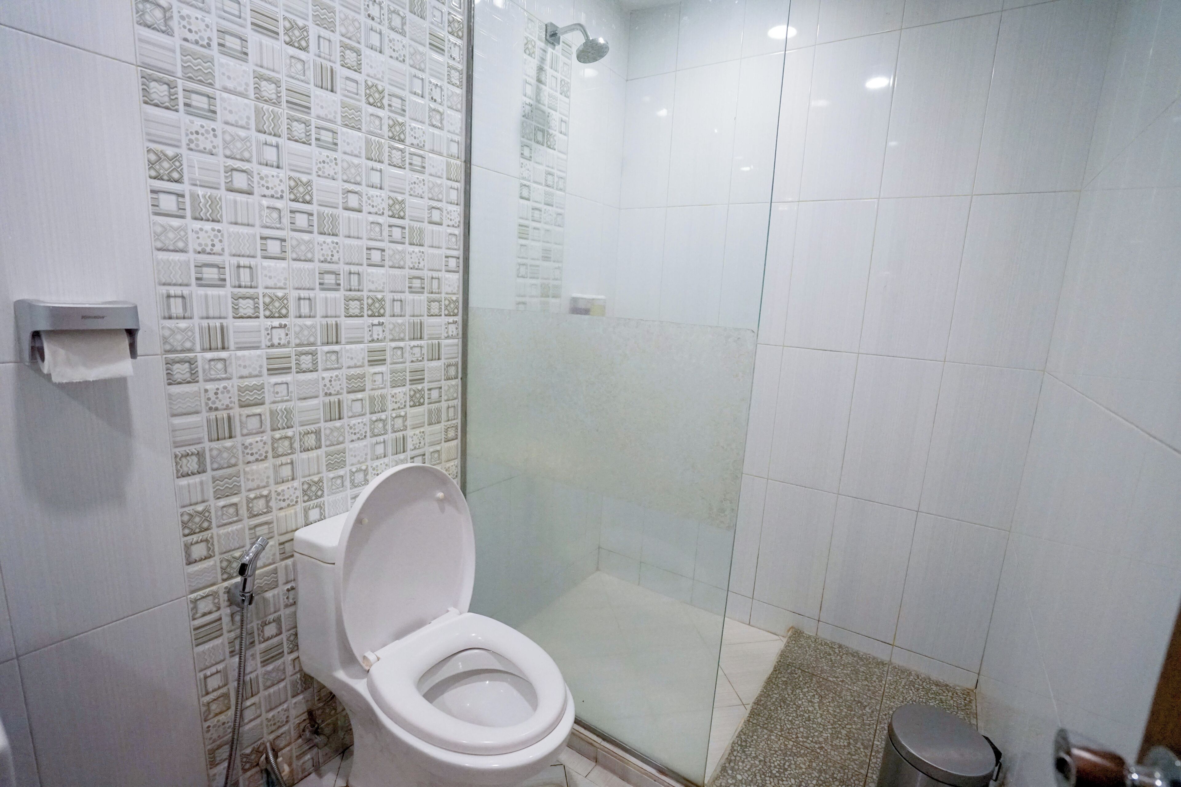 A bathroom with a toilet, a shower, and a patterned tile wall.