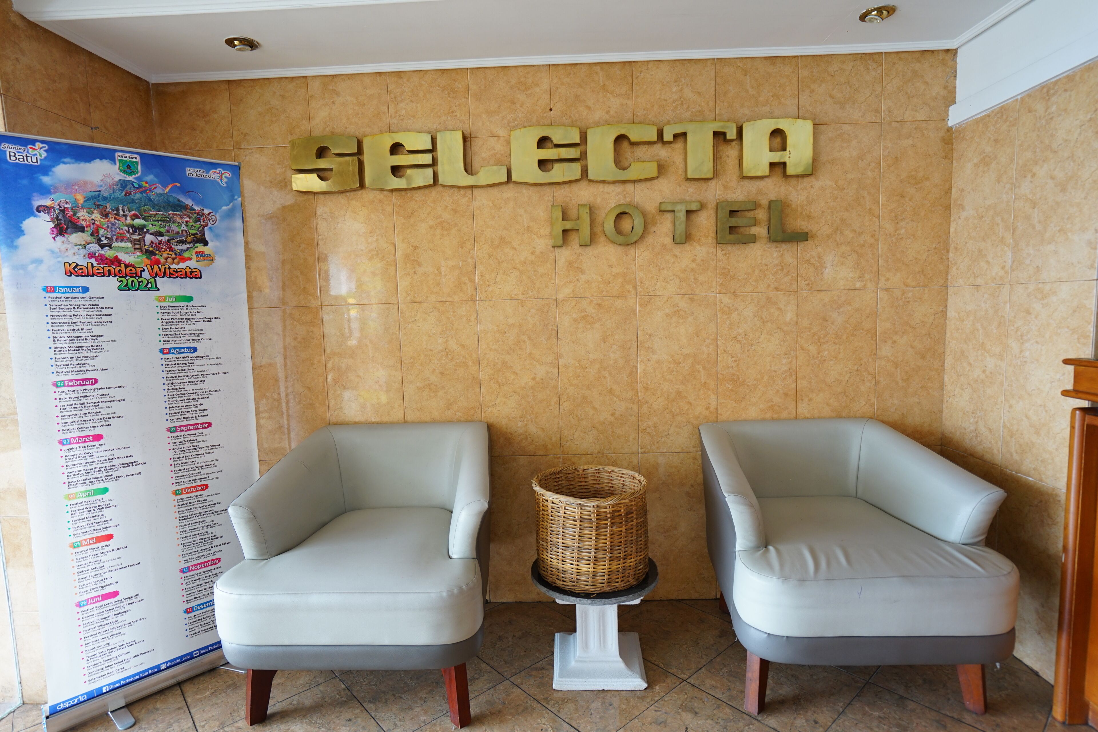 A reception area with two white armchairs, a small table with a wicker basket, and a wall with the words "SELECTA HOTEL" and a calendar.