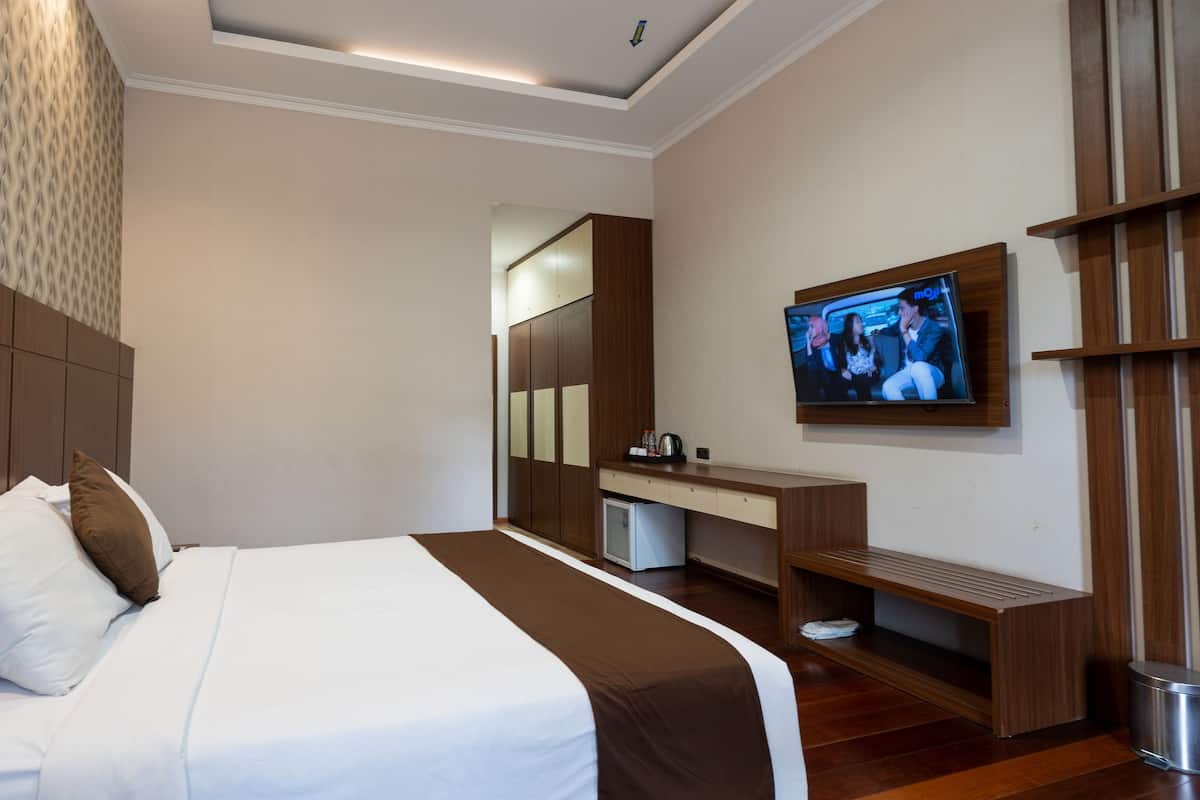 A hotel room with a large bed, a TV mounted on the wall, a desk with a mirror, and a wardrobe.