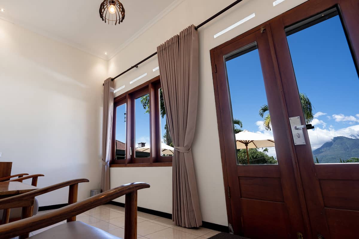 A hotel room with a wooden desk, chairs, a window with curtains, and a view of mountains.