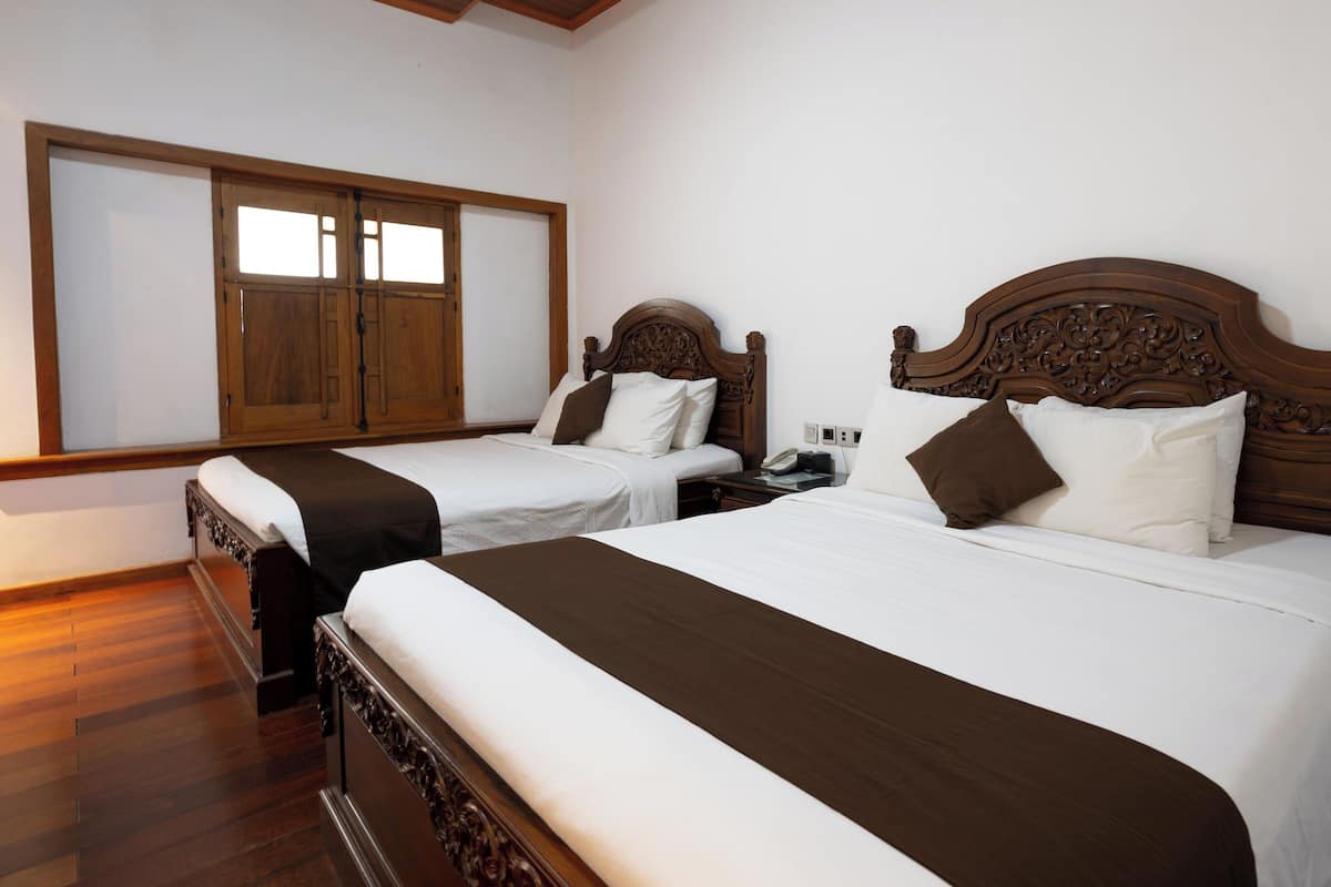 A hotel room with two beds, wooden headboards, white bedding, and a large window with wooden shutters.