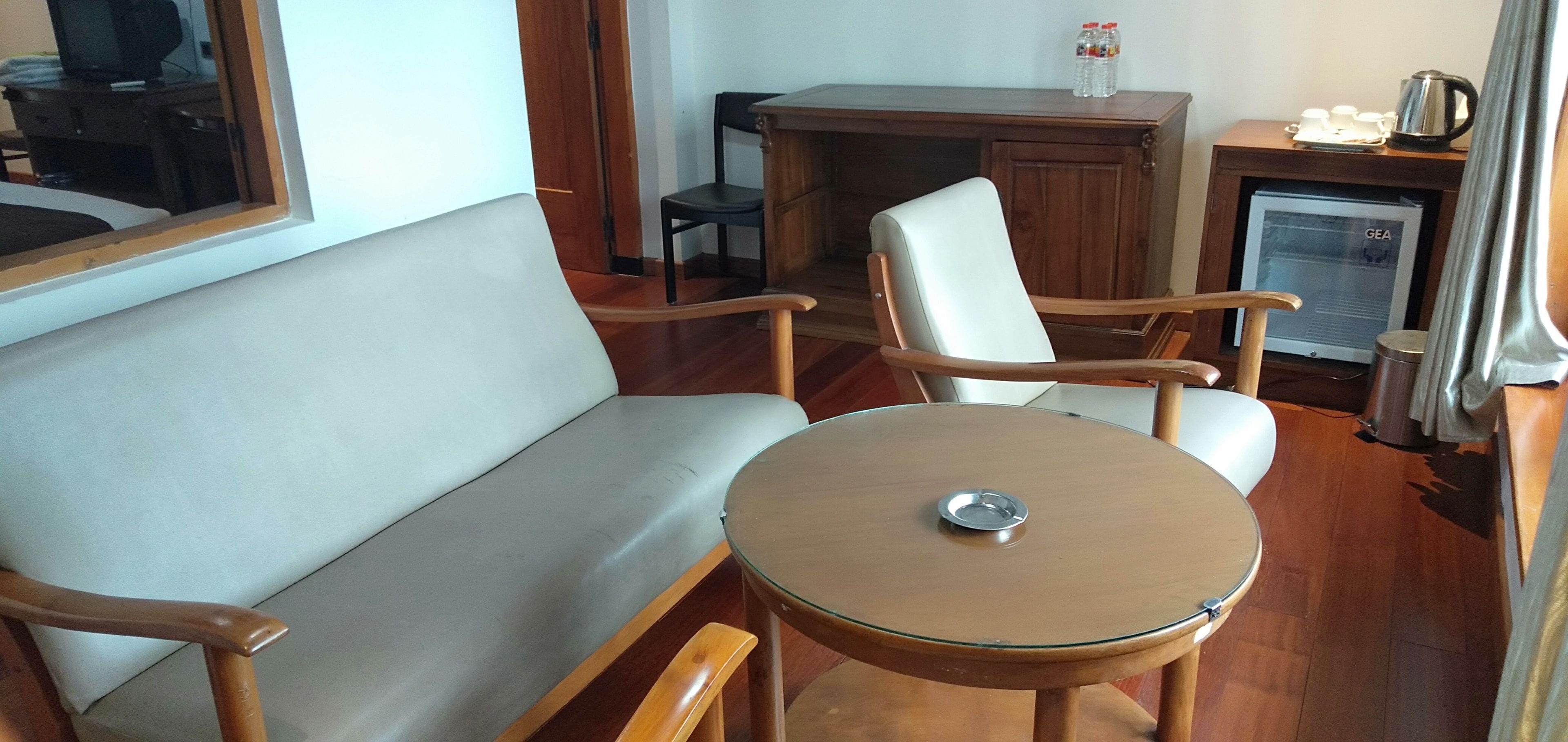 A compact room with a sofa, two armchairs, a small round table, a cabinet, a television, and a refrigerator.