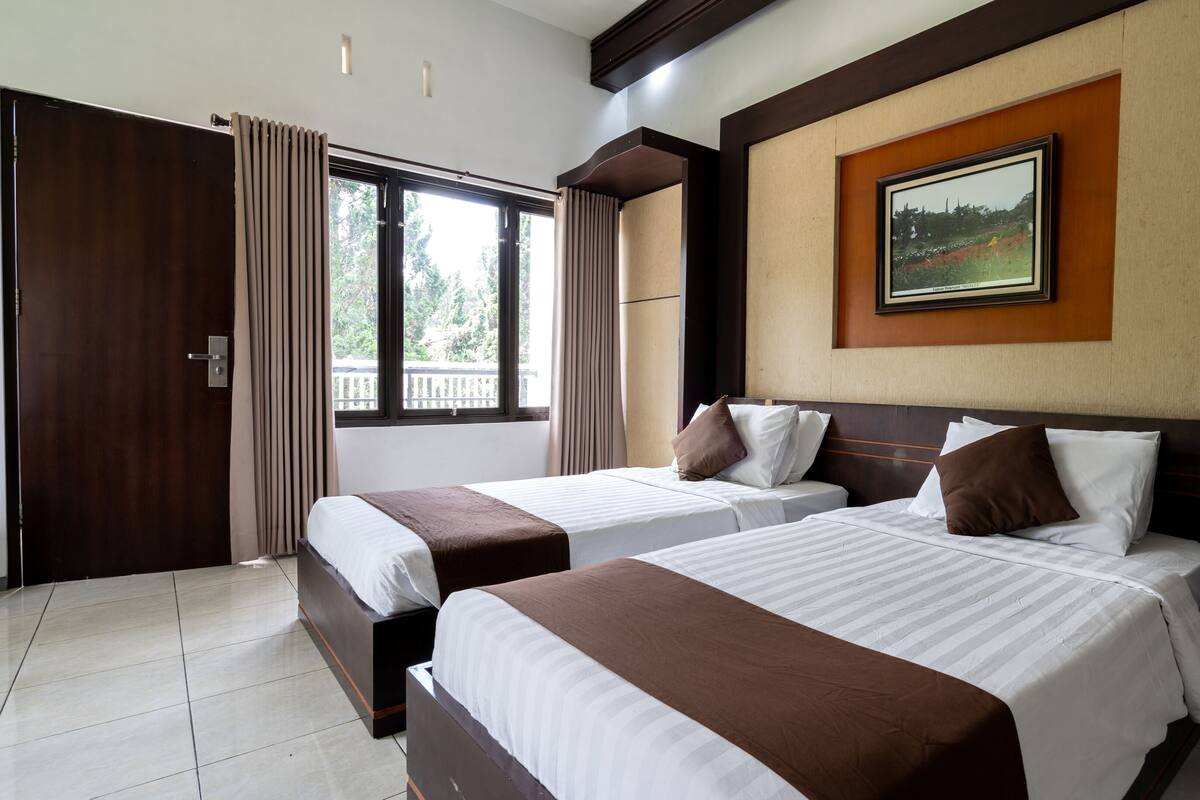 A hotel room with two beds, a large window, and a framed picture on the wall.