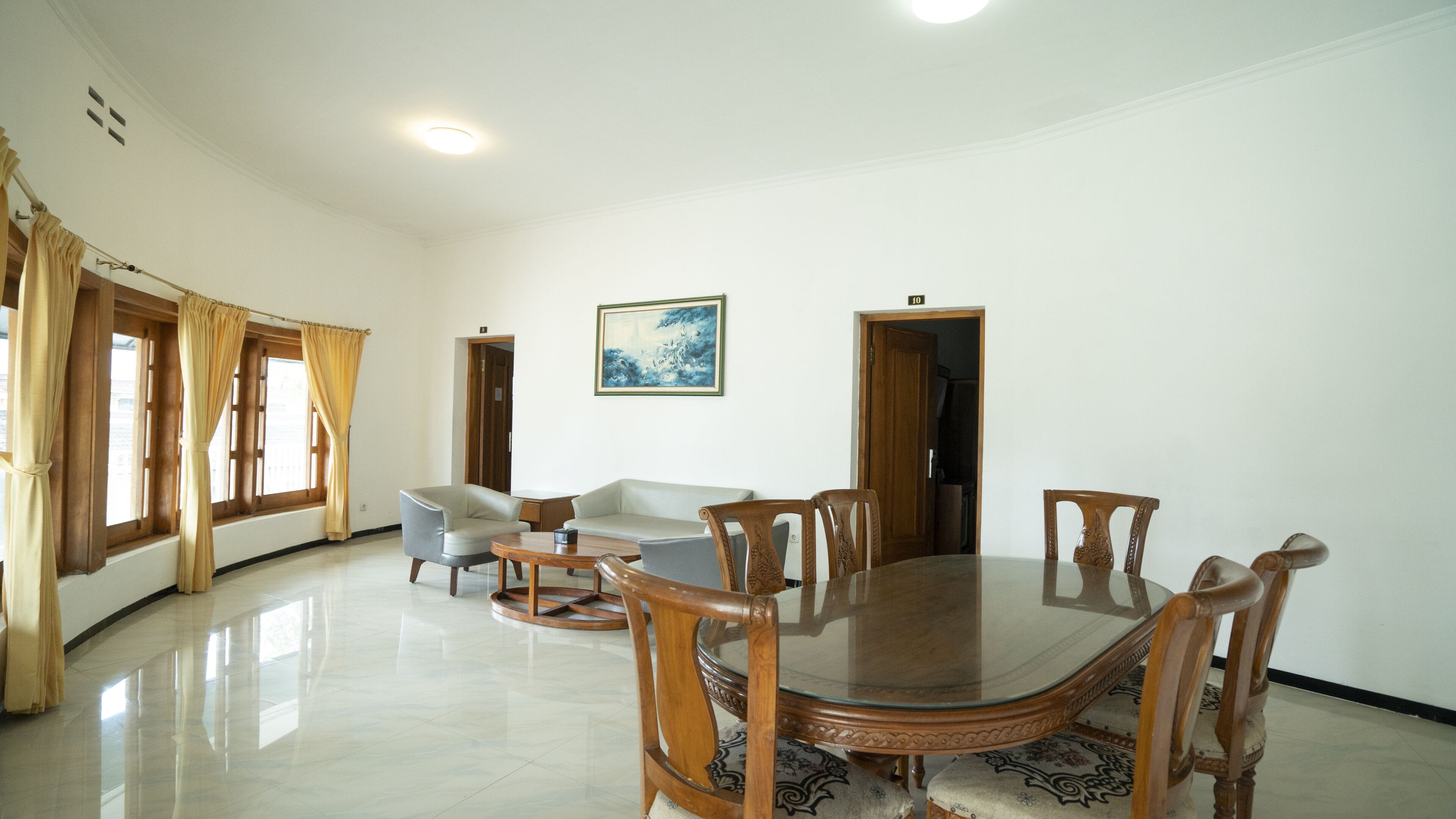 Een ruime kamer met een ronde houten tafel, verschillende stoelen, een bank en een schilderij aan de muur.