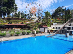 A swimming pool with a Ferris wheel in the background, surrounded by lush greenery and various buildings. - Hotel Selecta Batu Malang (Batu)