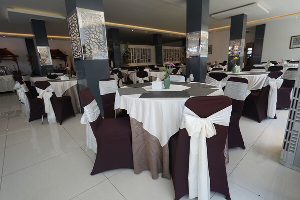 A banquet hall with round tables covered in white tablecloths and chairs with white and brown sashes.