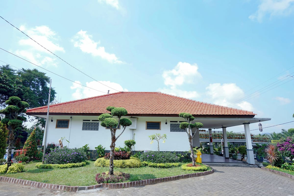 A white building with a red-tiled roof, surrounded by well-maintained gardens and a paved walkway.