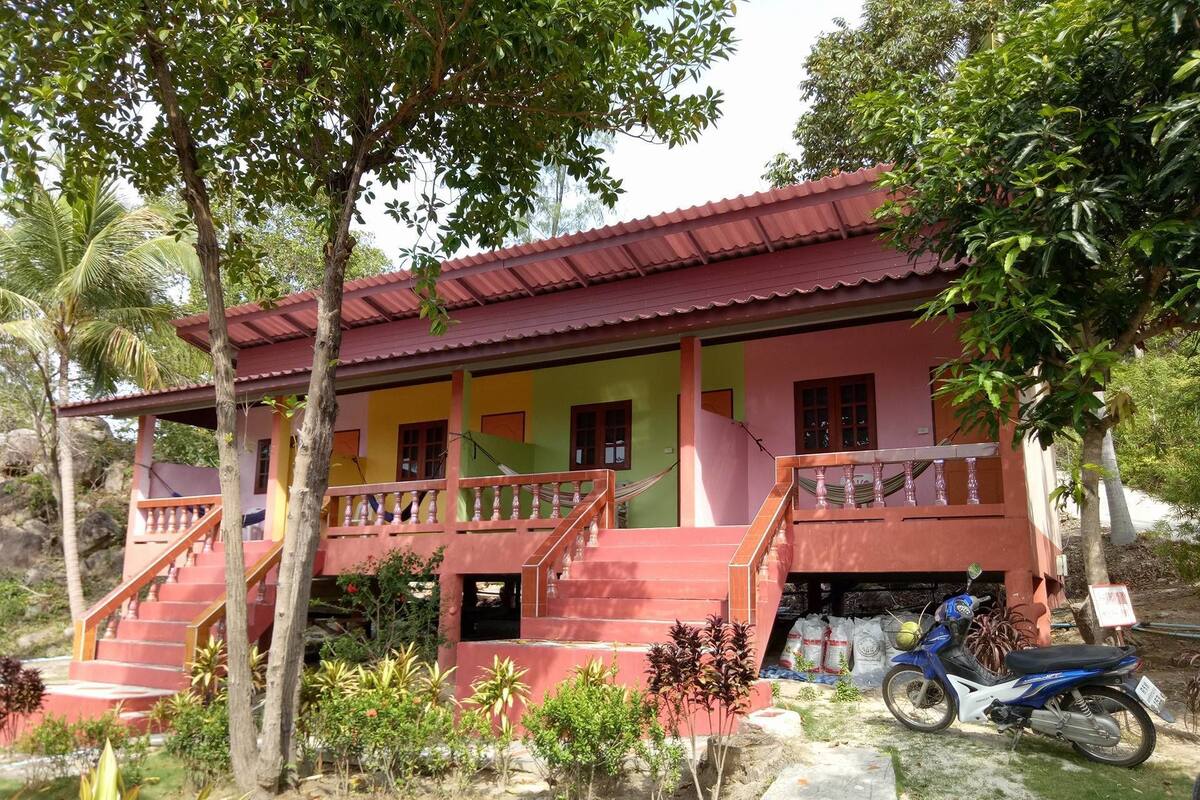 A two-story house with a red roof, a balcony, and a staircase leading to the upper floor.