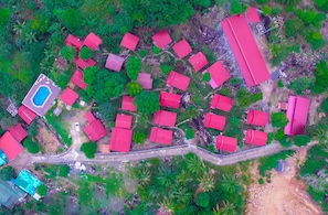 An aerial view of a residential area with multiple red-roofed houses, a swimming pool, and a winding road.