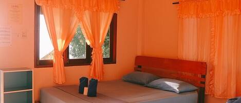Habitación con dos camas, cortinas anaranjadas, cabecera de madera, suelo de baldosas y unidad de aire acondicionado.