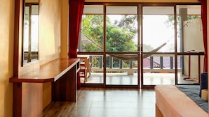 Amplia habitación con un gran ventanal corredero que da a un balcón, un banco de madera y una cama con edredón azul.