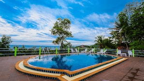 Una piscina con borde de azulejos, rodeada por una valla baja y sillas de descanso blancas.