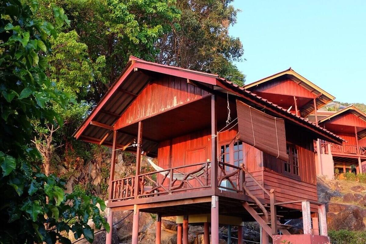 A wooden cabin with a balcony, surrounded by trees and rocks.