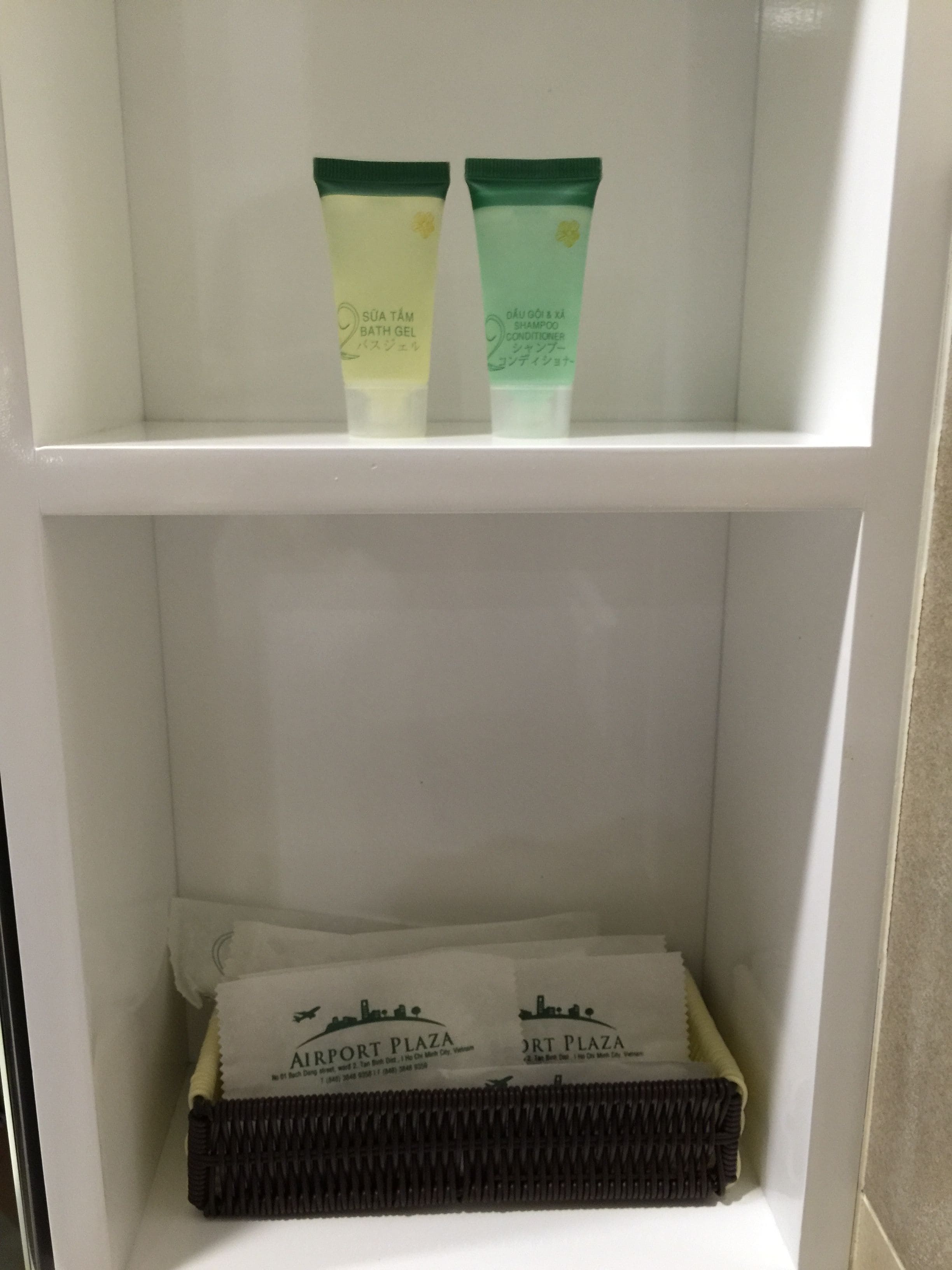 A bathroom shelf with two bath gels and two Airport Plaza branded towels.