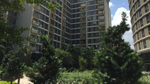 Een meerlaags woongebouw met balkons, omgeven door weelderige begroeiing.