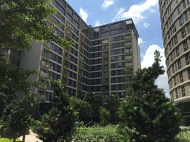 Um edifício residencial com várias andares e varandas, rodeado por vegetação exuberante.