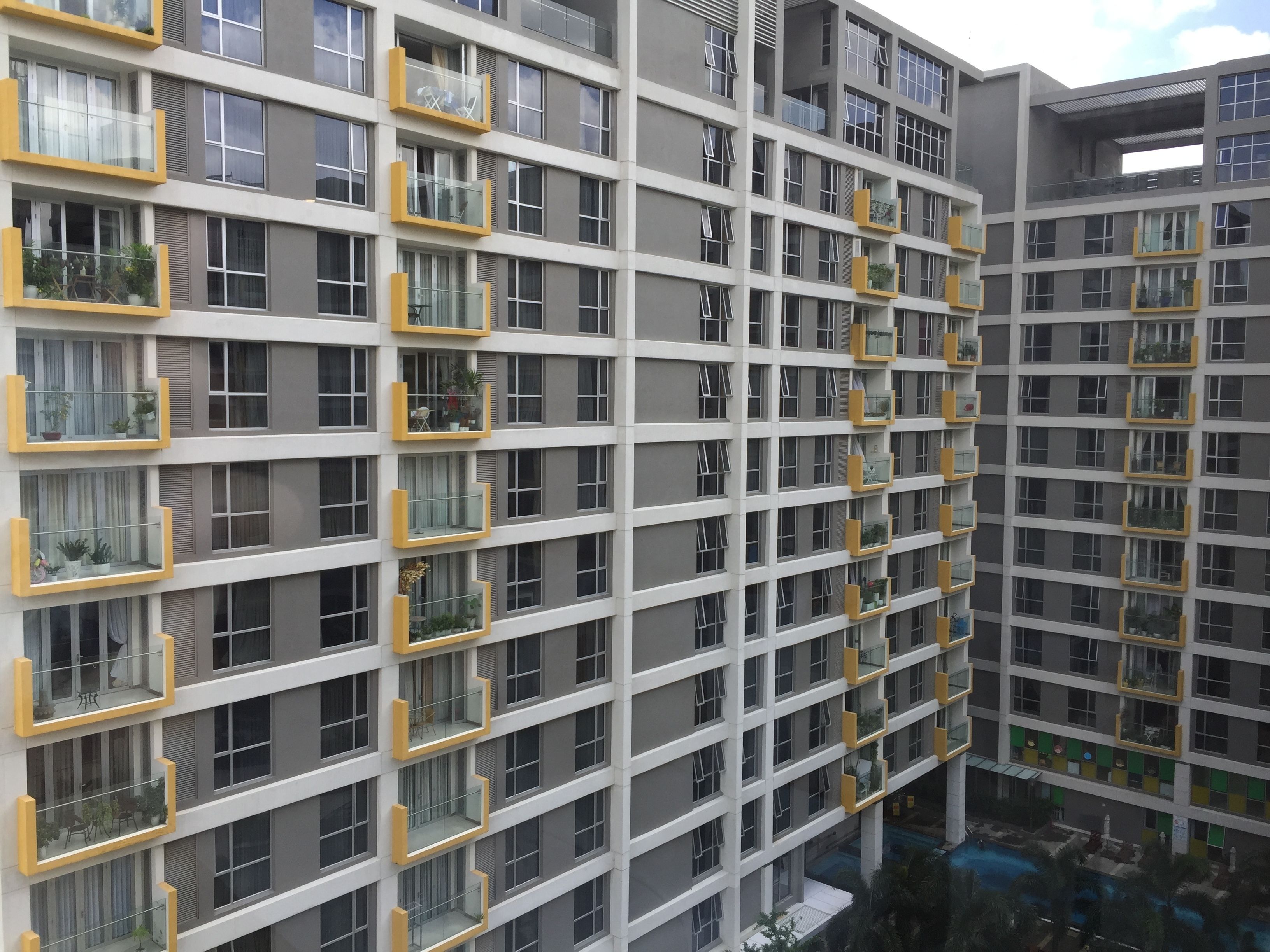 Un immeuble résidentiel à plusieurs étages, doté de balcons, de grandes fenêtres et d’une cour avec une piscine.