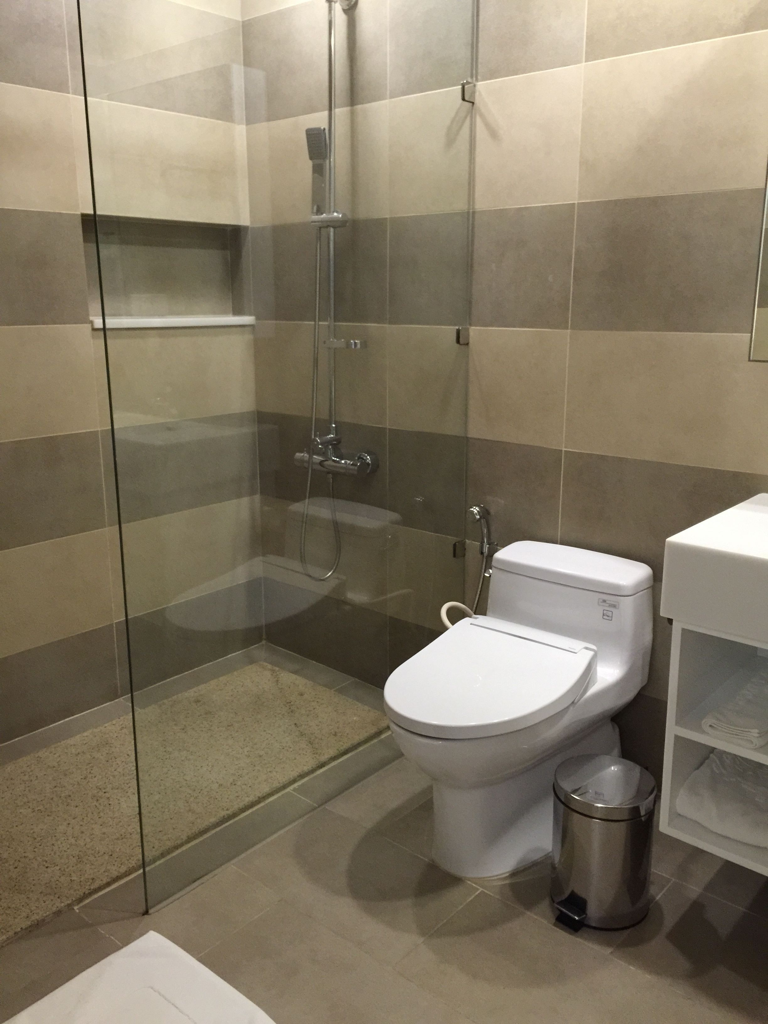 A modern bathroom with a glass-enclosed shower, a white toilet, and a stainless steel trash can.