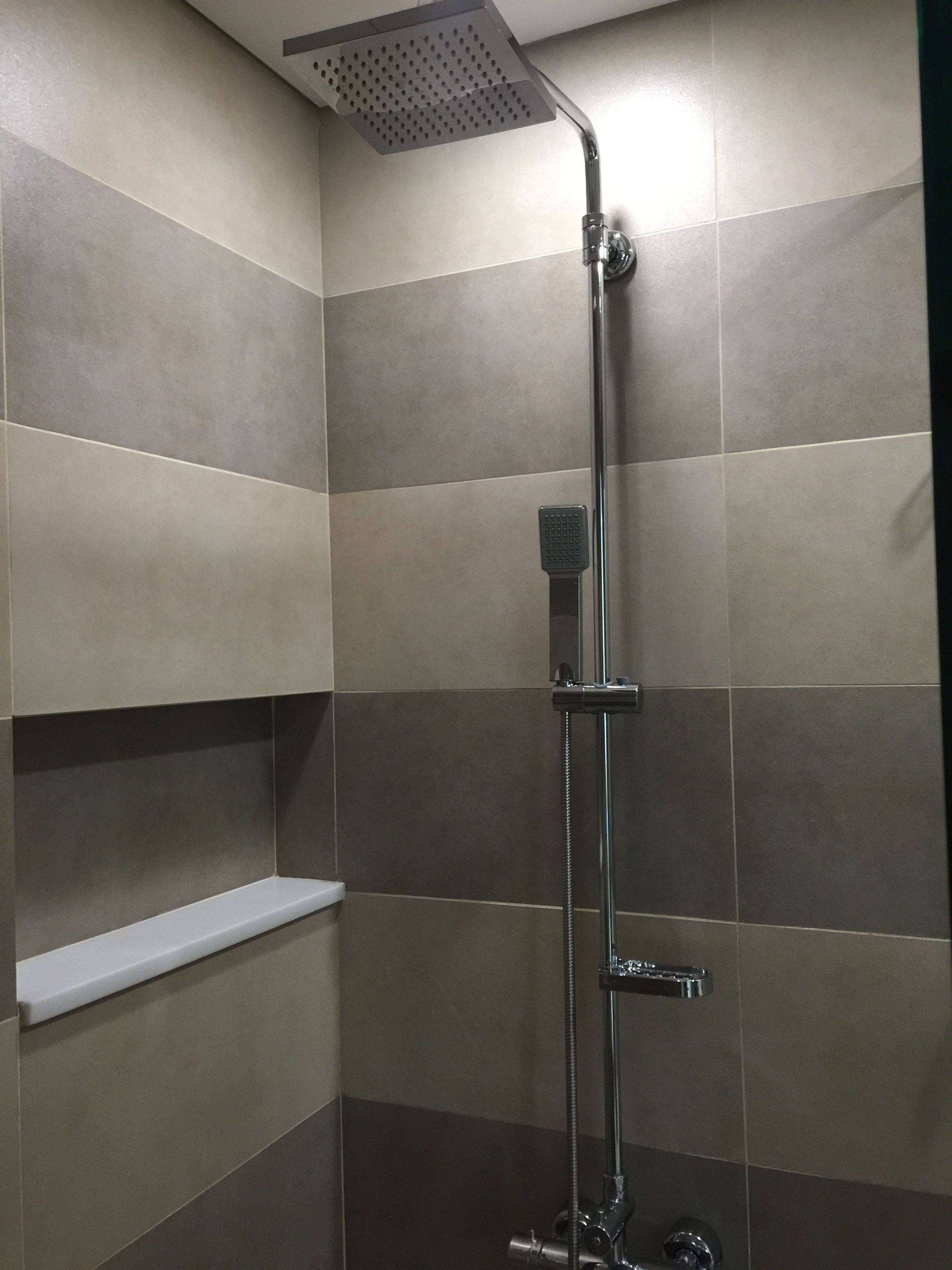 A shower with a handheld showerhead, a handheld soap dispenser, and a wall-mounted control panel.