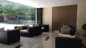 Een moderne lobby met zwarte banken en stoelen, grote ramen met uitzicht op groen buiten, en een betegelde muur.