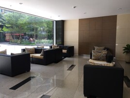 Um hall moderno com sofás e cadeiras pretas, grandes janelas com vista para o verde exterior e uma parede revestida de azulejos.