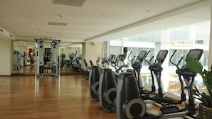 Een fitnessruimte met trainingsapparaten, een spiegelwand en grote ramen.
