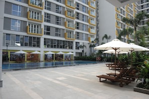 A modern building with multiple balconies, a swimming pool, and outdoor seating areas with umbrellas.