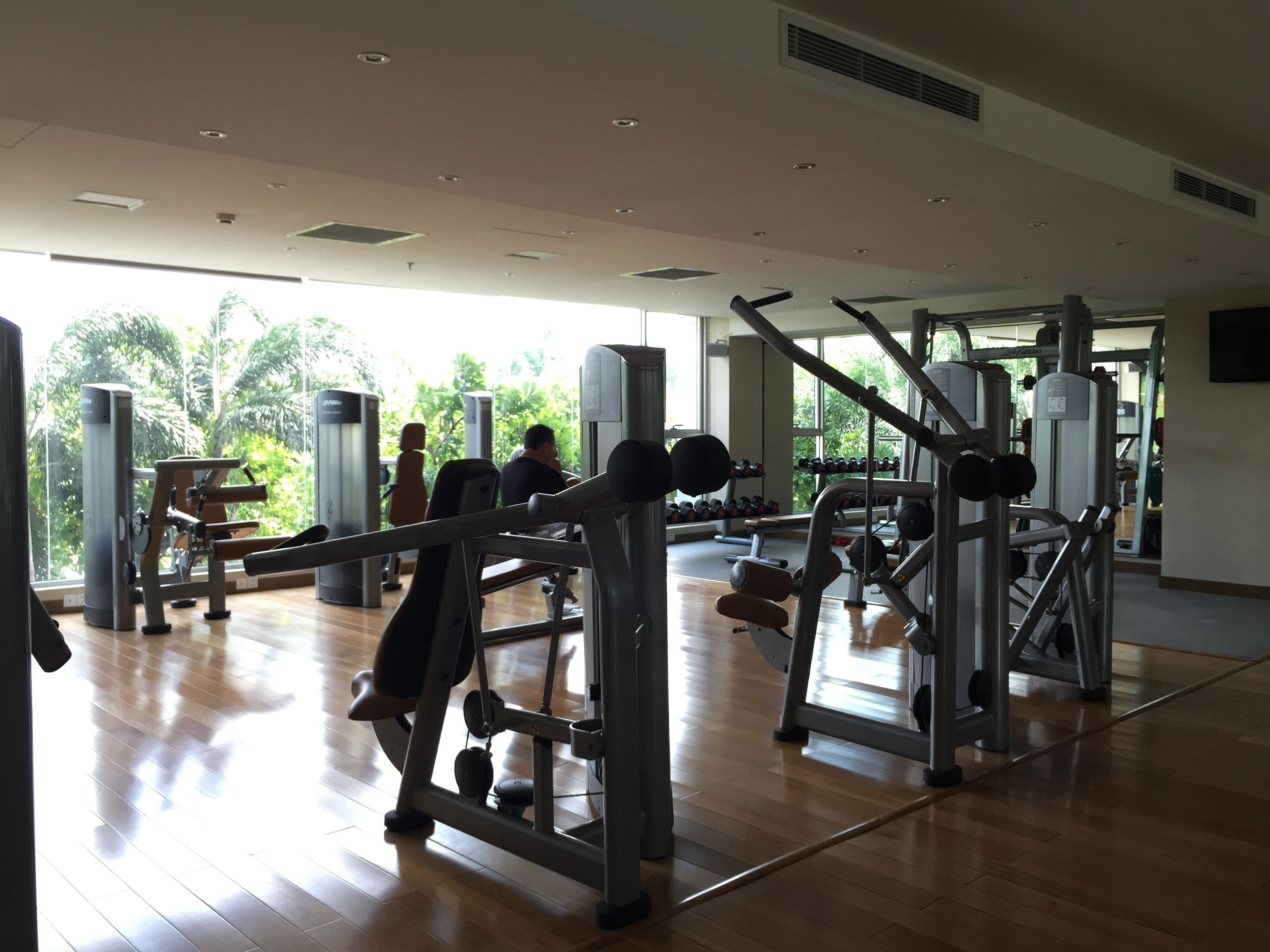 Une salle de sport équipée de divers appareils d’exercice, dotée de grandes fenêtres et d’un plancher en bois.