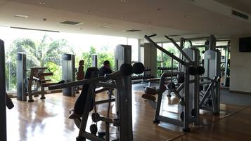 Une salle de sport équipée de divers appareils d’exercice, dotée de grandes fenêtres et d’un plancher en bois.