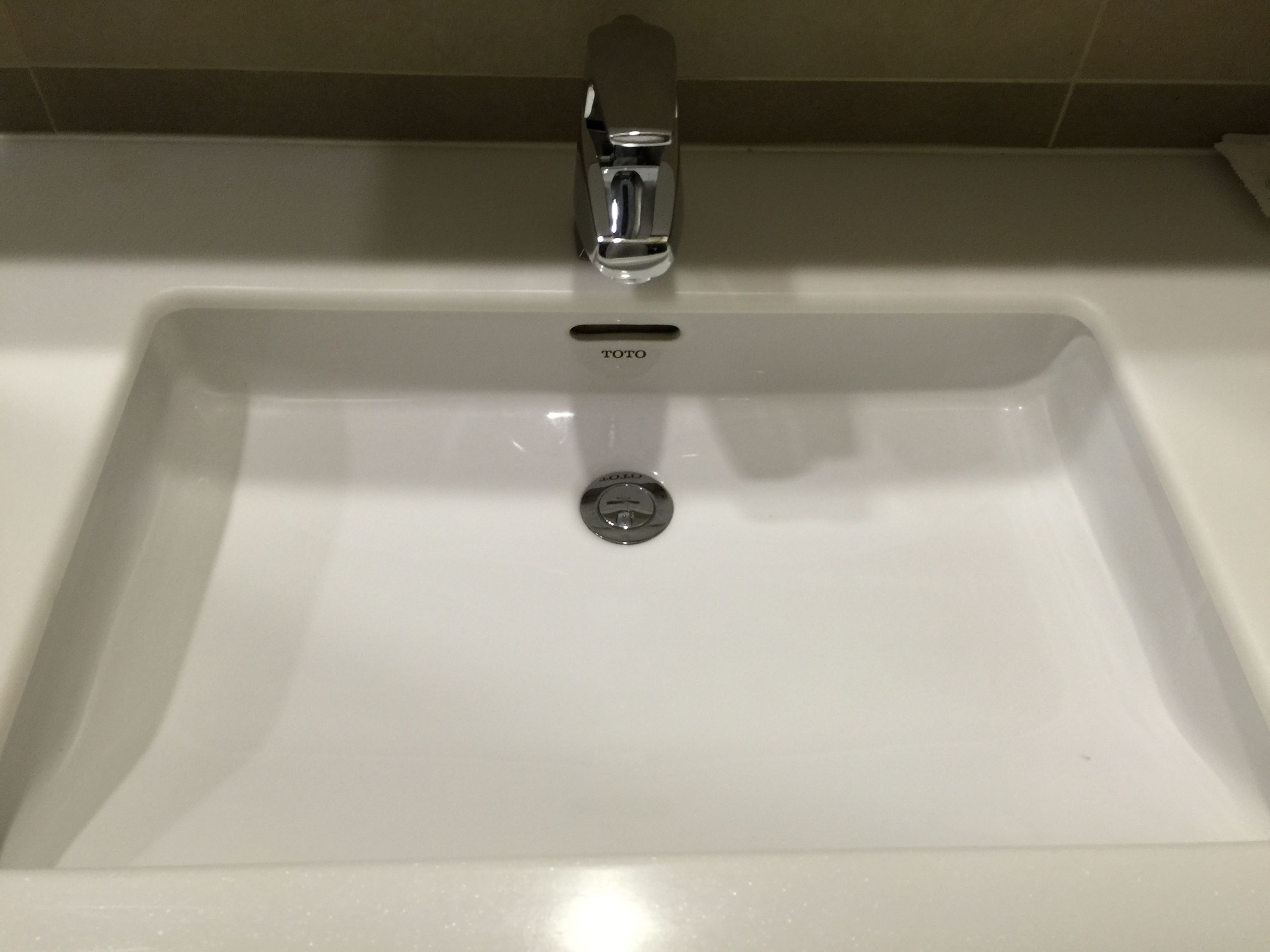 Un lavabo de salle de bain blanc, doté d’un robinet chromé et d’un bouchon de vidette de la marque Toto.