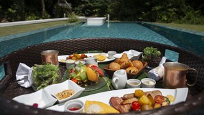A dining table with a variety of food items and drinks, set by a poolside with lush greenery in the background. - Jusandi (Ishigaki)