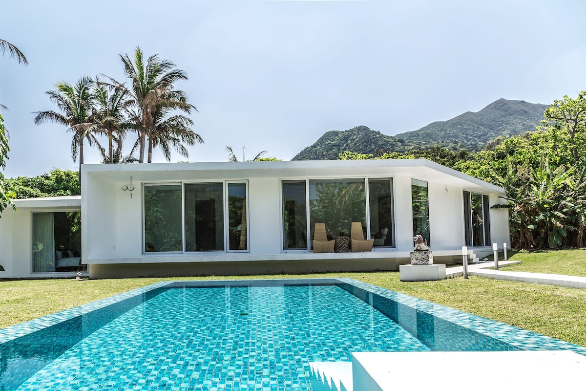 A modern house with a swimming pool, large windows, and a view of mountains.