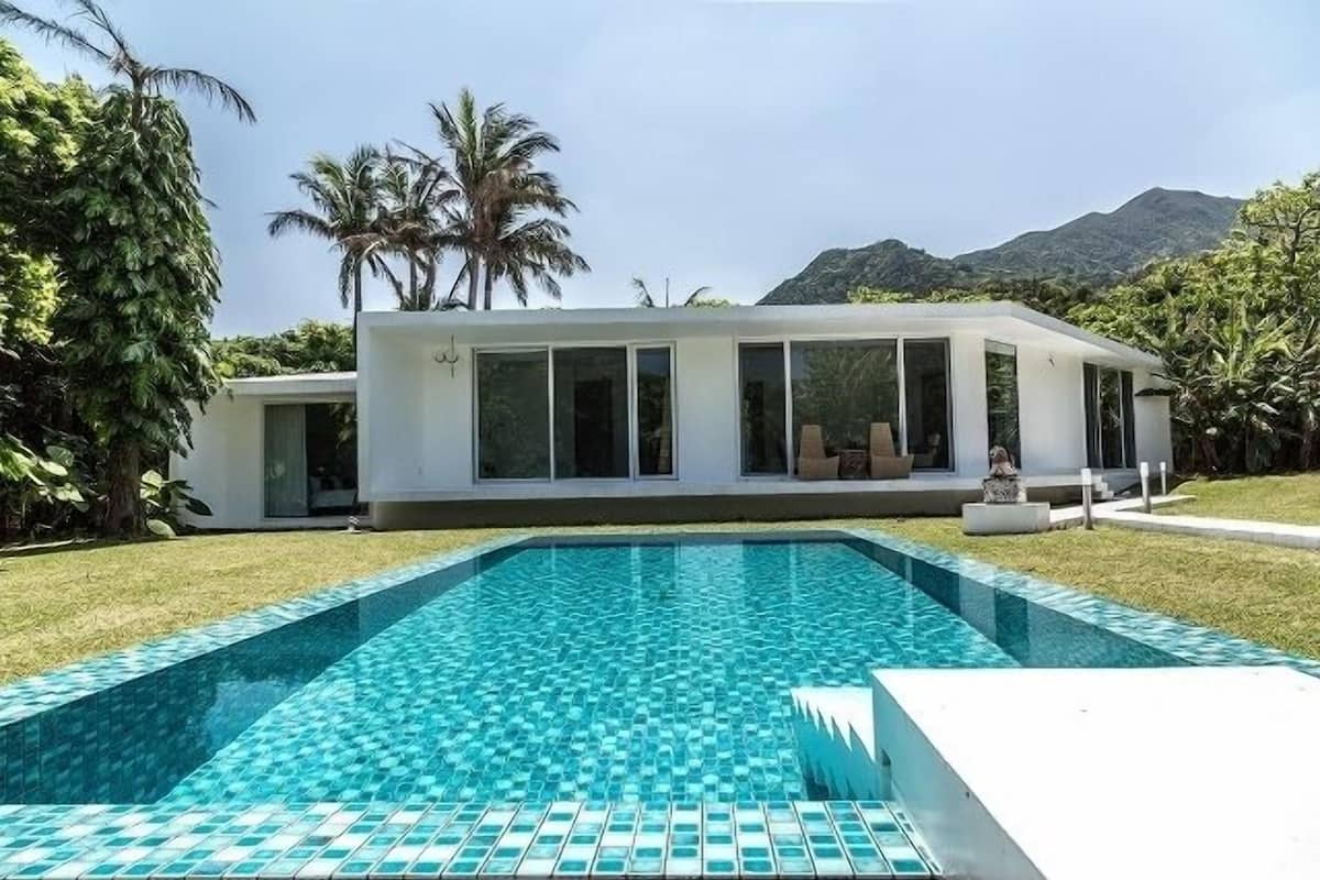 A modern house with a swimming pool, large windows, and a view of mountains.