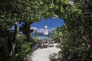 An outdoor seating area with two chairs and a table, surrounded by lush greenery and overlooking a clear blue ocean. - Jusandi (Ishigaki)
