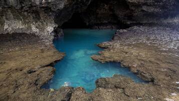 Eine natürliche Höhle mit einem klaren, blauen Pool, umgeben von felsigem Gelände.