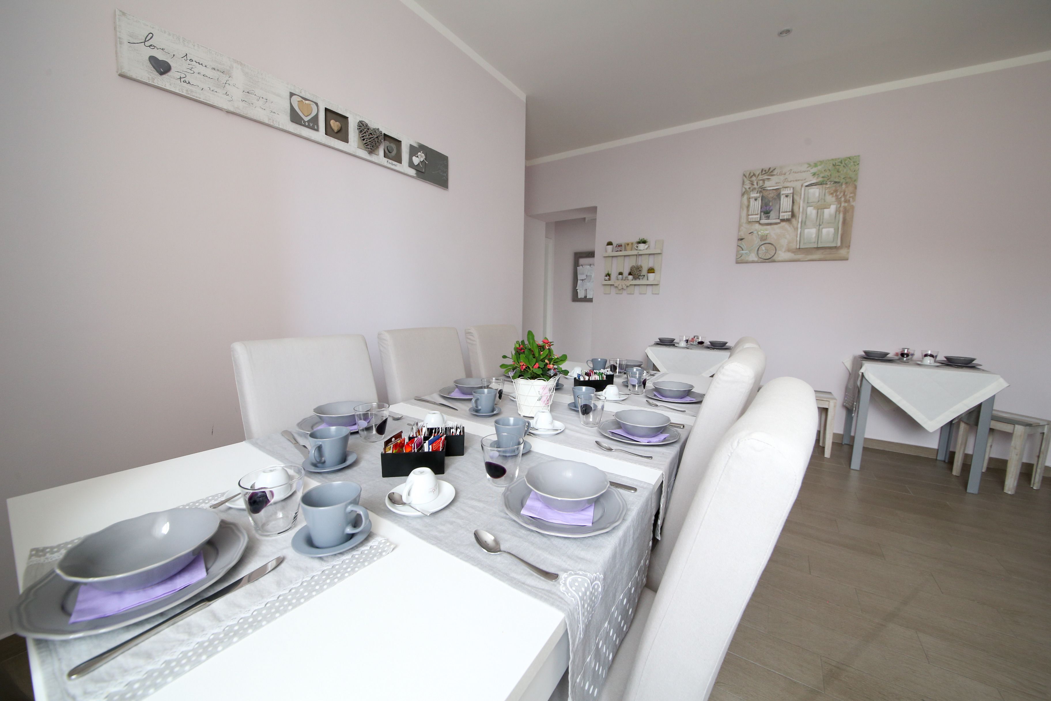 A dining area with a long table set for a meal, chairs, and a small side table with a vase of flowers.