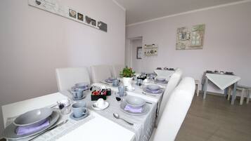 A dining area with a long table set for a meal, chairs, and a small side table with a vase of flowers.