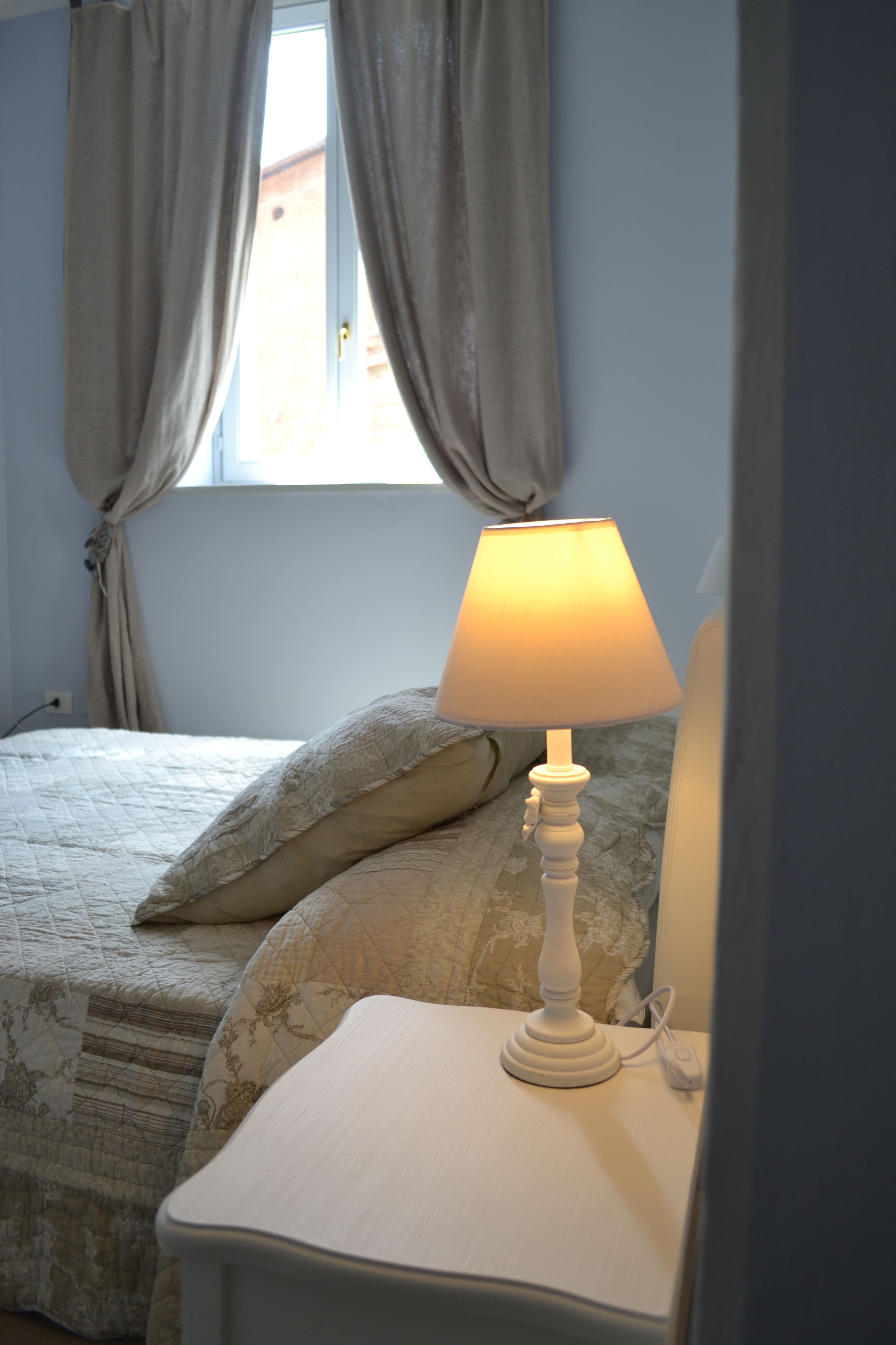 A bedroom with a bed, a bedside table with a lamp, and a window with curtains.