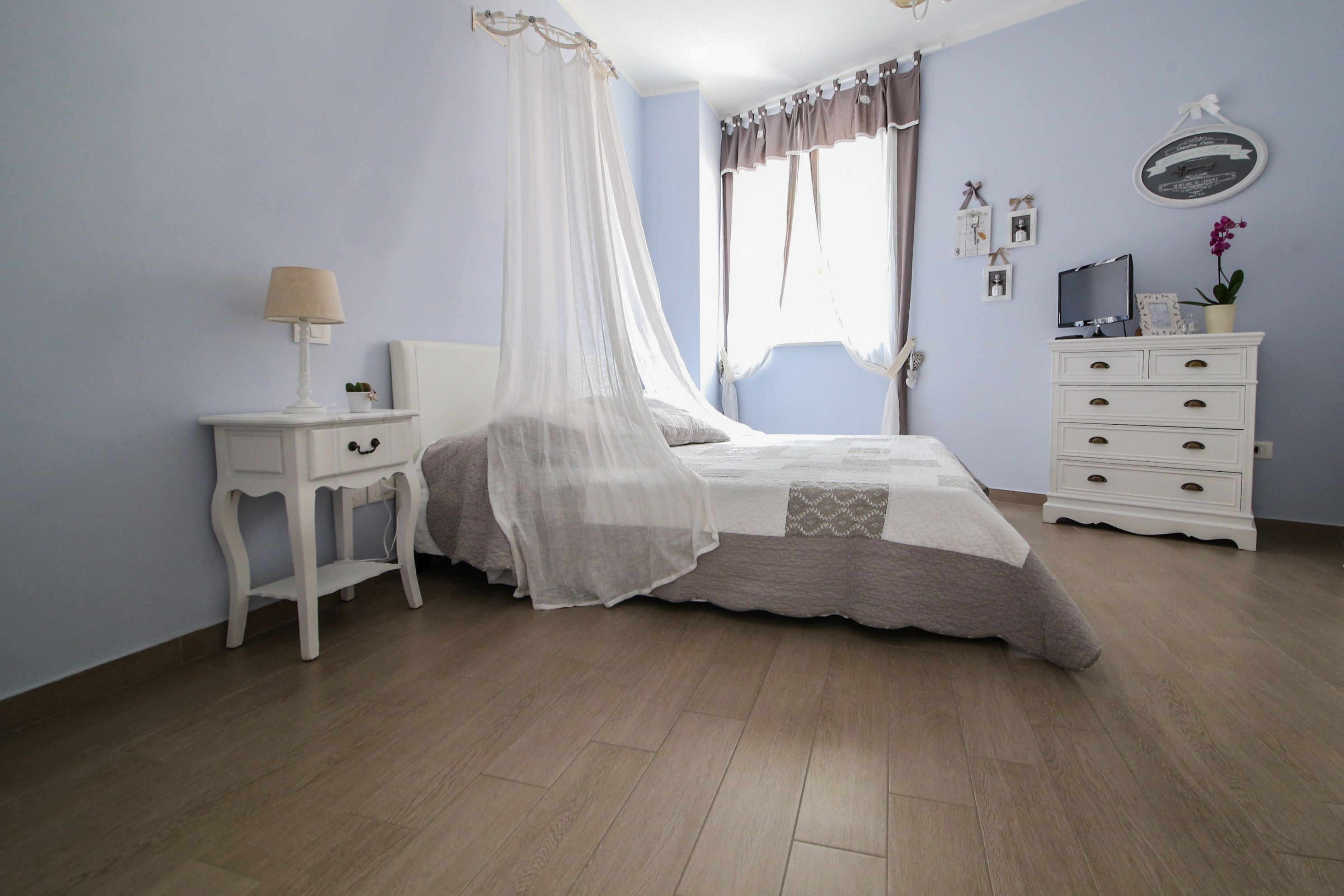 Un dormitorio con cama, mesita de noche, cómoda y ventana con cortinas.