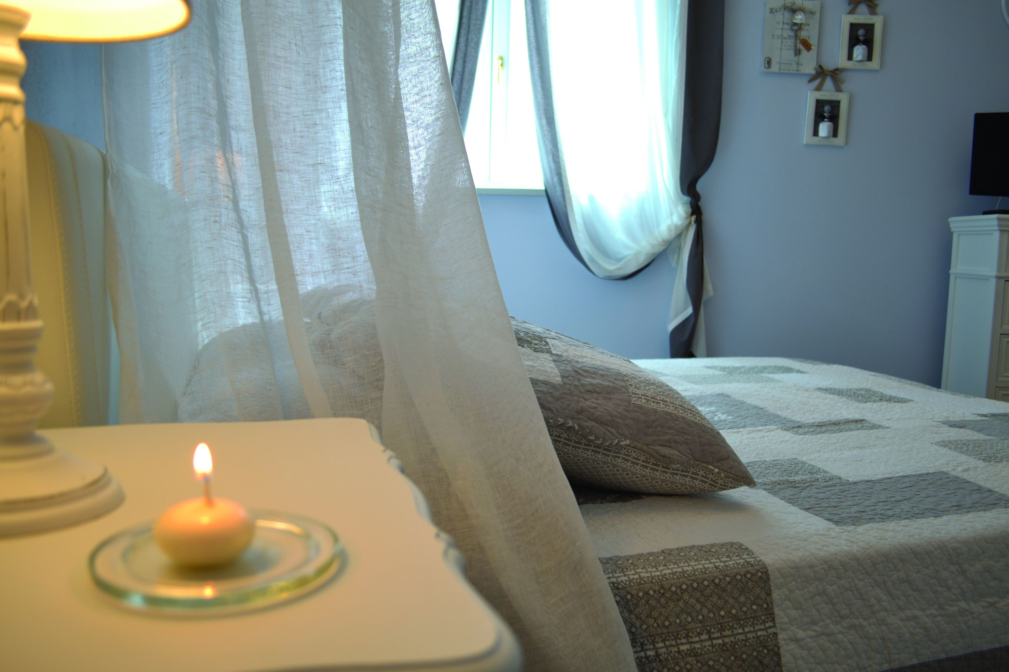 A bedroom with a bed, a bedside table with a candle, and a window with curtains.