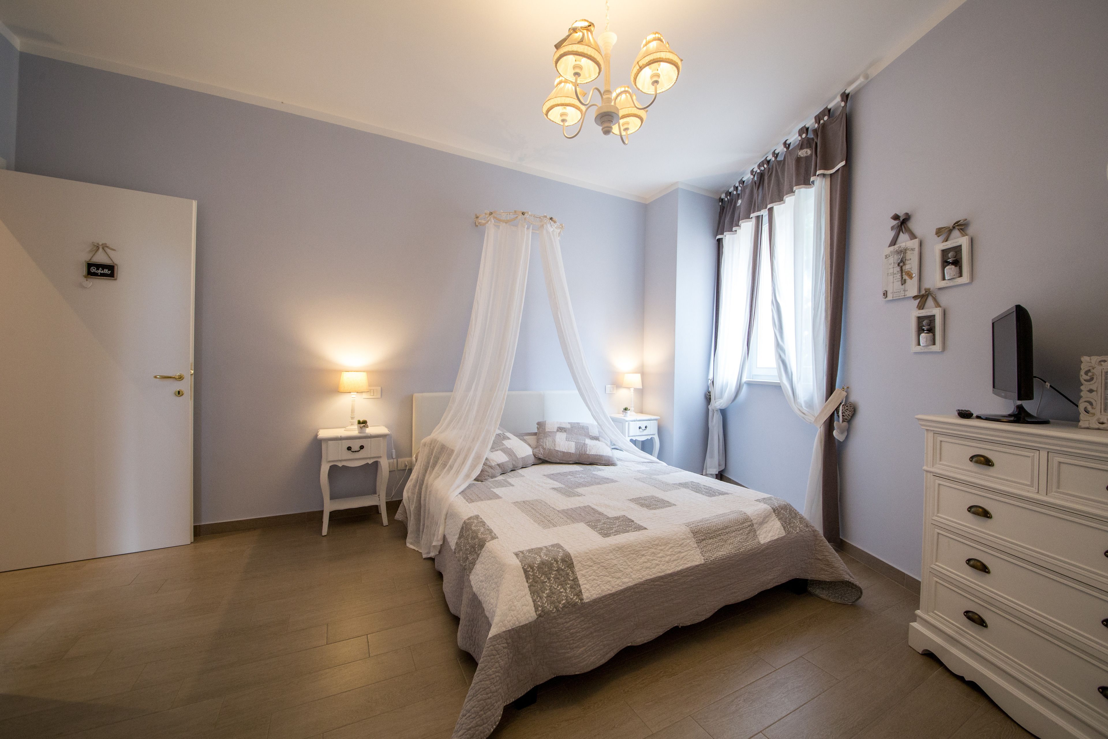 Une chambre à coucher avec un lit, des tables de chevet, une commode, un lustre et des rideaux.