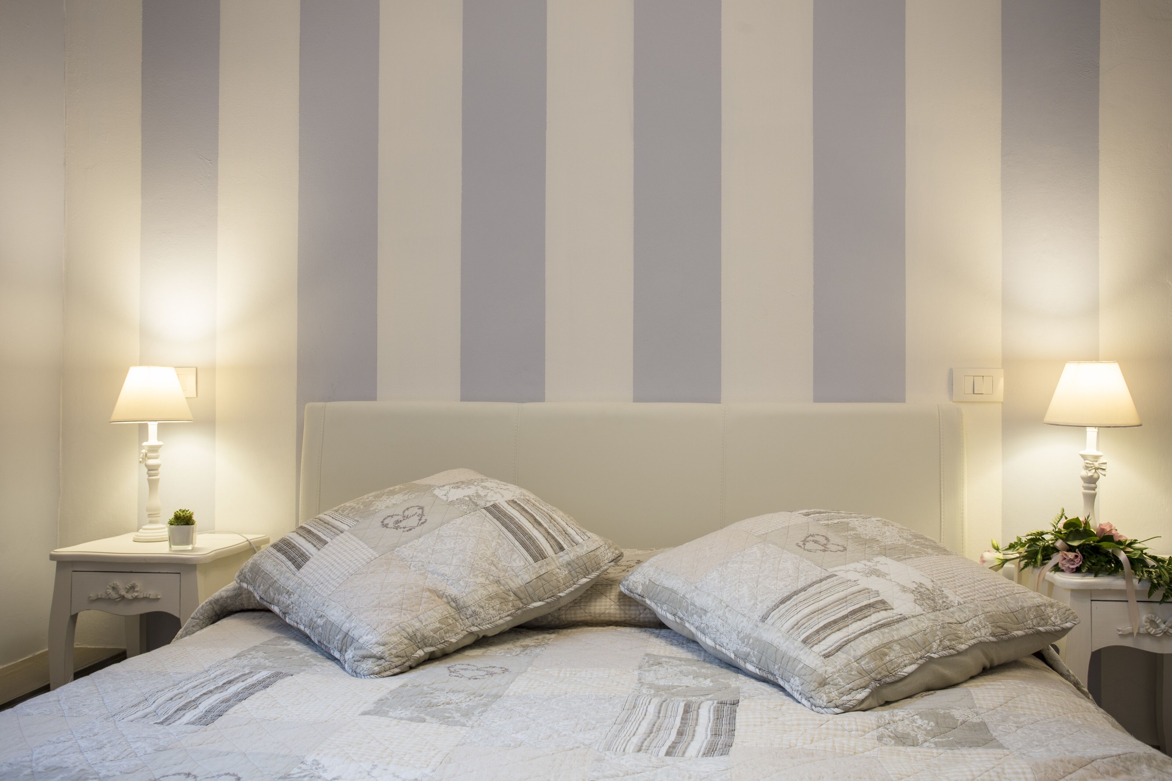 A neatly made bed with two pillows, a bedside table with a lamp, and a wall with vertical stripes.