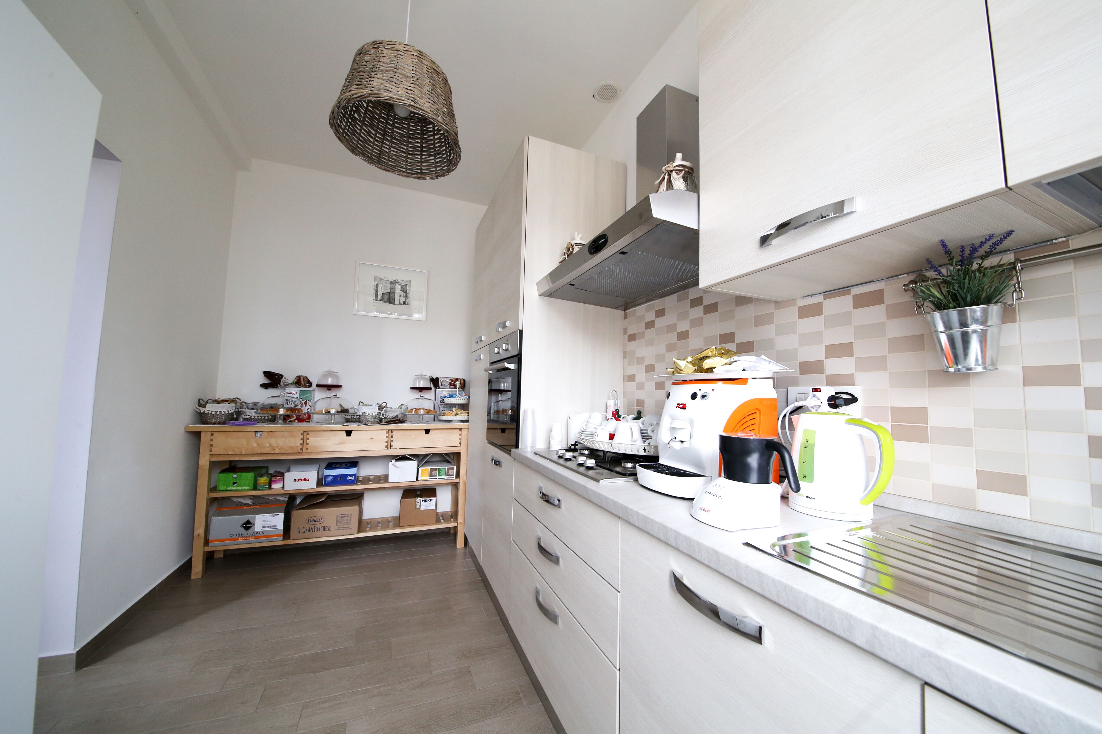 Une cuisine moderne avec des meubles blancs, un plan de travail en bois et divers appareils électroménagers, notamment une machine à café et une bouilloire.