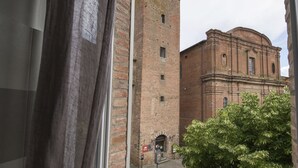 A view through a window with a curtain, revealing a brick building with a tall tower and a smaller building with a dome.
